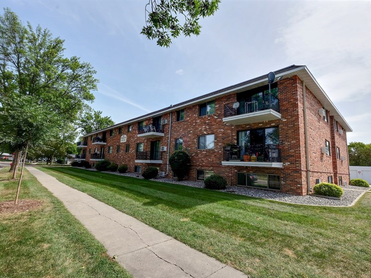 the exterior of a brick apartment building with a sidewalk and grass. Fargo, ND Martha Alice Apartments
